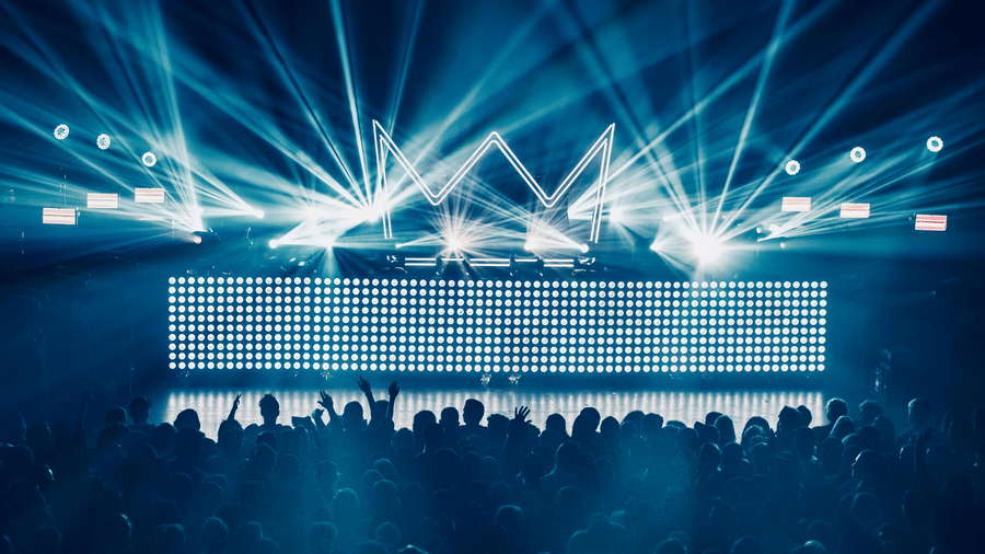 Silhouette of people raising hands while facing a stage with sharp lights
