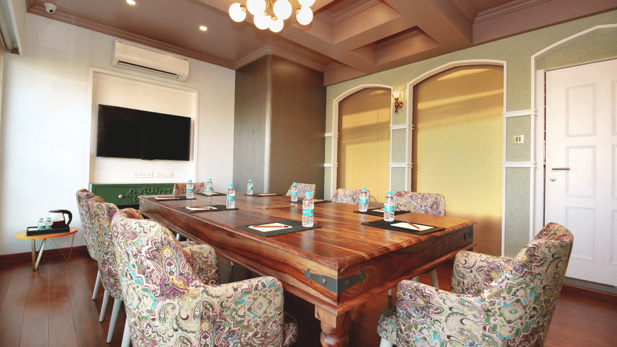 A boardroom near BKC at Theory9 - Premium Serviced Apartments, Bandra, featuring a rectangular table and plush chairs around it with a TV mounted on the wall at one end