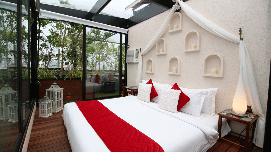 A bed beautifully set up in an open-air space, surrounded by an enchanting view with nature and sky above offering a refined accommodation in Bandra West, at Theory9 - Premium Serviced Apartments