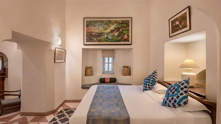 A bedroom with a bed, a window seat, and wall art in Tijara Fort-Palace - 19th Century, Alwar.