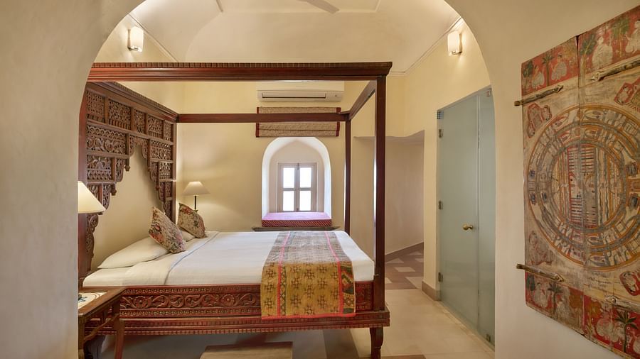 Room with four-poster bed, patterned runner, arched alcove with window, lamp, artwork, and doorway - Tijara Fort-Palace - 19th Century, Alwar.