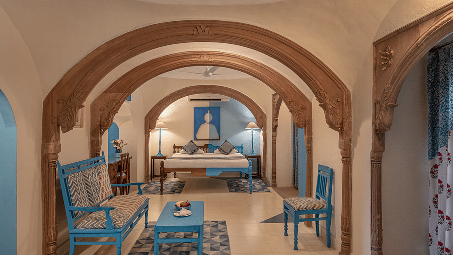A room with a bed, a sofa, chairs, a table, and multiple arched doorways in Tijara Fort-Palace - 19th Century, Alwar.