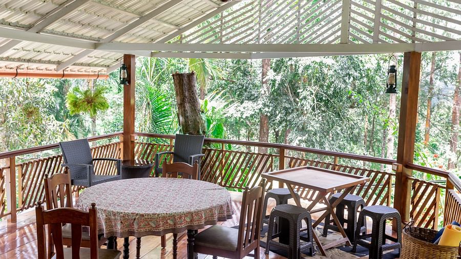 A deck with tables, chairs, and carror board with a lush green background.
