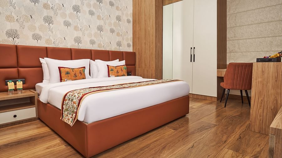 A large king size bed with pillows, wardrobe, a coffee table and chair at Triptam Hotel, Vrindavan