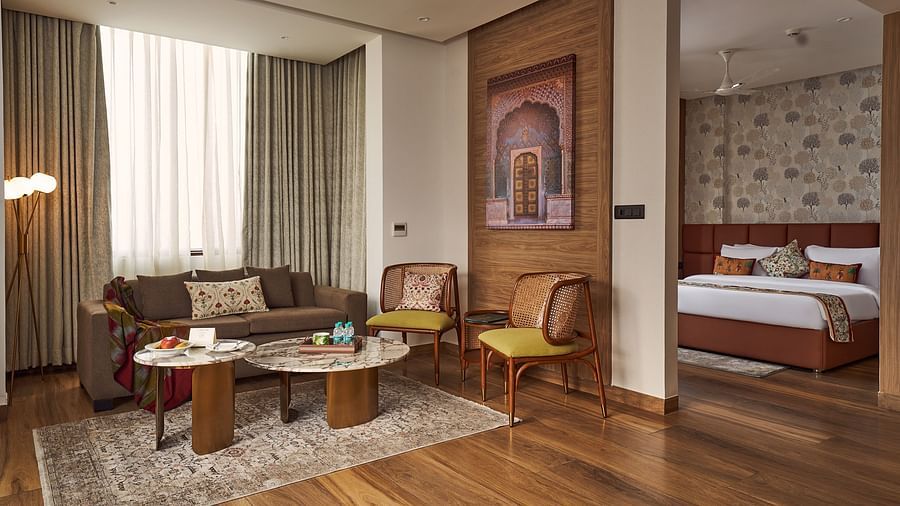 Interior of the room with intricate wooden decors, and seats alongside wall paintings, with a view of a well decorated room with a king bed at Triptam Hotel, Vrindavan