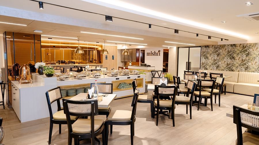 interior of the restaurant at Triptam Hotel, Vrindavan with multiple 4 seater setting with tbales and wooden chairs in a vibrant room