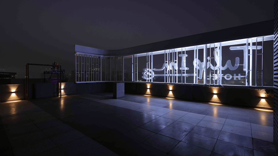A night view of the Tulip Inn Gurugram rooftop terrace featuring a modern illuminated glass railing and warm floor lighting.