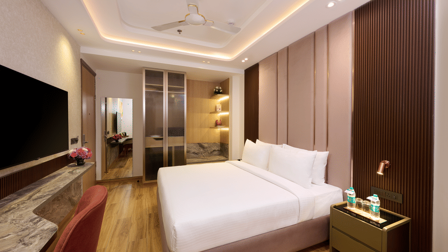 A bedroom at Tulip Inn Gurugram with wooden flooring, a large bed, a wall-mounted TV, and a workspace with a chair.