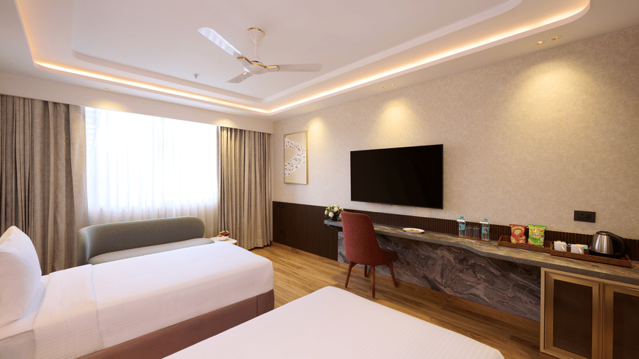 Interior view of a Tulip Inn Gurugram bedroom featuring twin beds, a wall-mounted flat-screen TV, and a long wooden storage console.