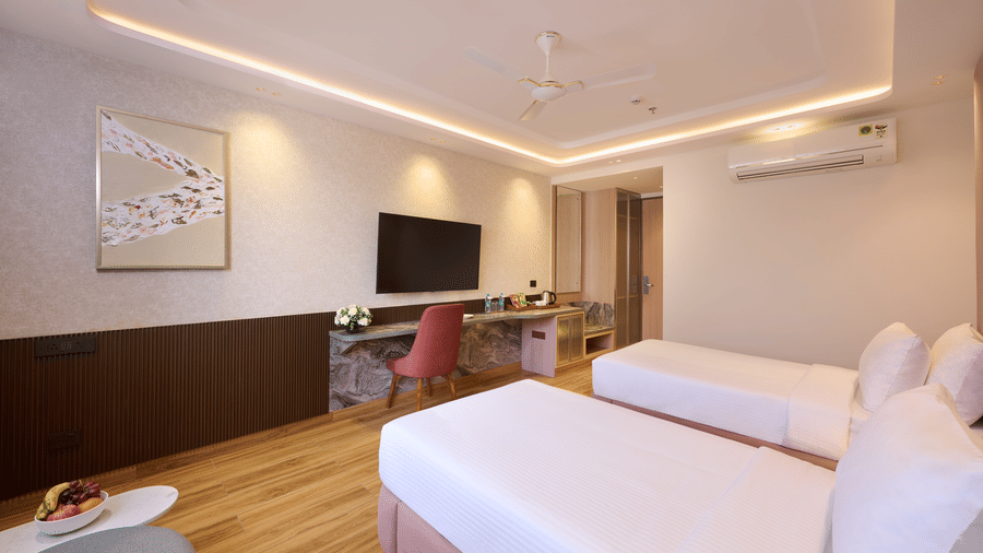 Wide shot of a guest room at Tulip Inn Gurugram displaying twin beds, wood flooring, a desk area, and a large abstract painting on the wall.