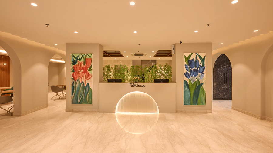 Interior of the Tulip Inn Gurugram lobby showing a marble reception desk flanked by 2 large floral wall murals.