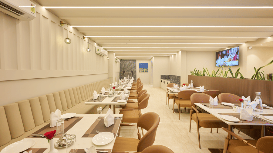 A restaurant dining room at Tulip Inn Gurugram with long rows of set tables, chairs, and a linear light-panelled ceiling.