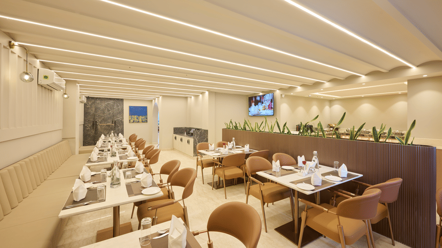 Dining area at Tulip Inn Gurugram featuring tables with cloths, chairs, and a partition with indoor greenery.