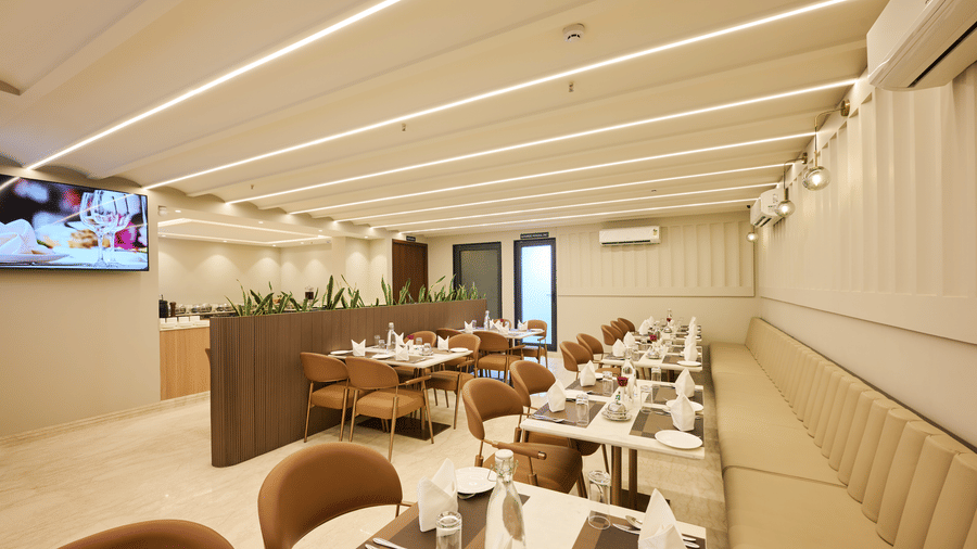 Wide view of the Tulip Inn Gurugram dining room featuring structured ceiling lights, furniture, and a television screen.