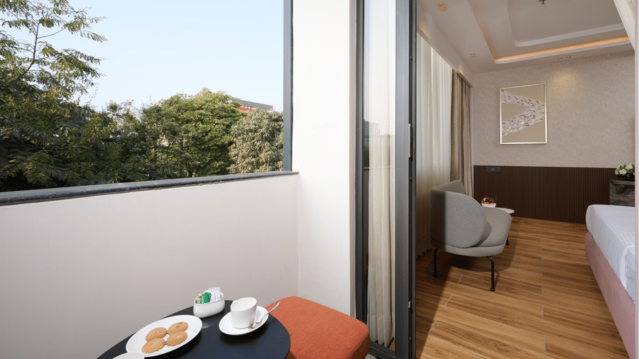 A private seating area at Tulip Inn Gurugram with a small table, stools, and a view of trees through glass sliding doors.