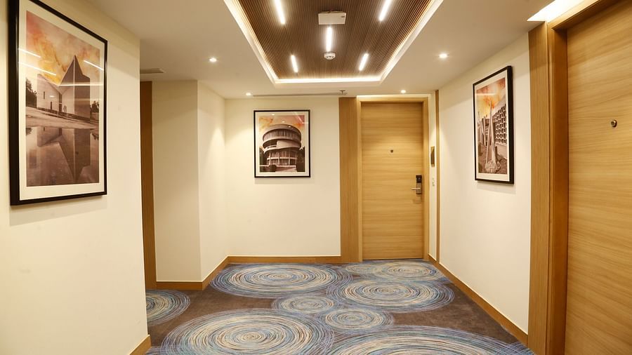 An image of the corridor leading to the hotel rooms with carpeted flooring and walls with paintings - Tulip Inn, Zirakpur