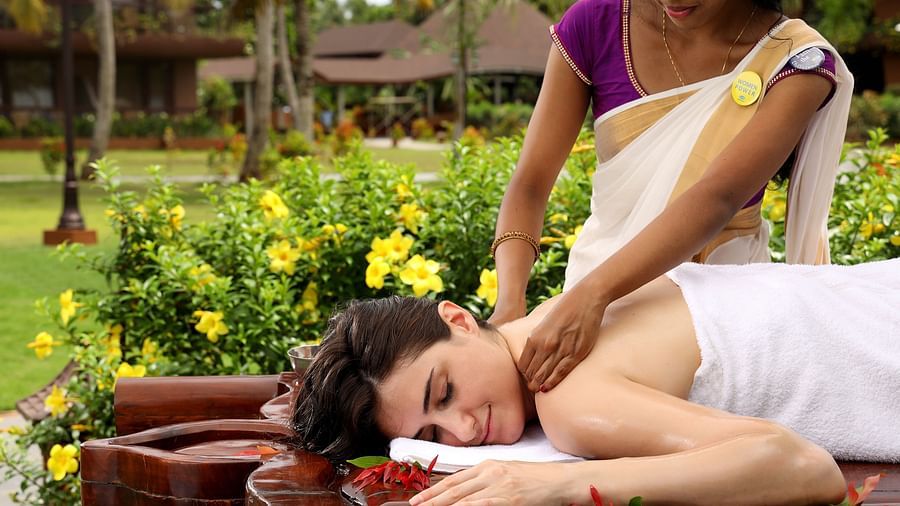 A woman receiving a relaxing neck and shoulder massage while lying on her stomach outdoors at Ayurveda Spa, Uday Backwater Resort