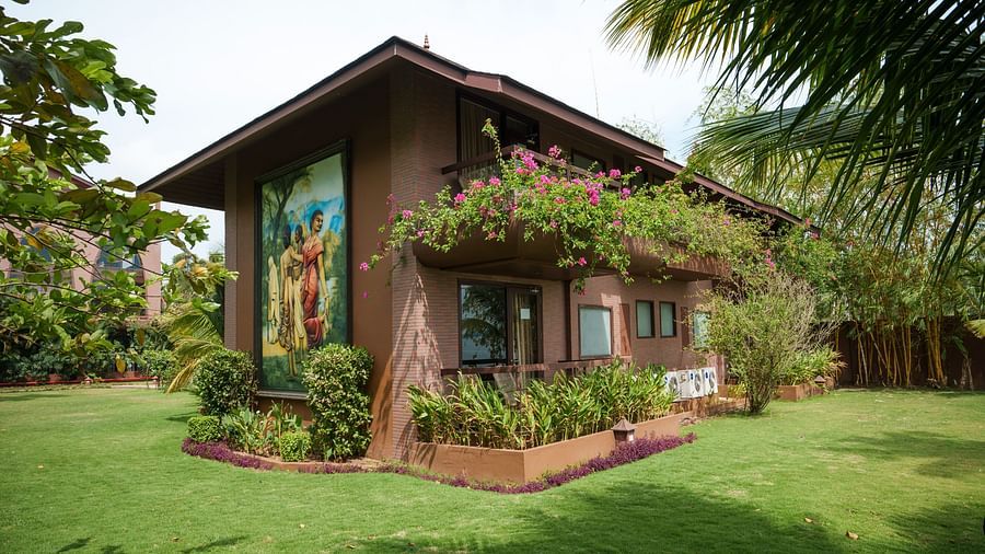 Facade of a villa at Uday Backwater Resort on a sunny day amidst lush lawn and bougainvilleas flourishing from the balcony