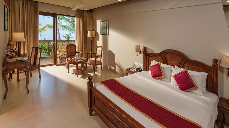 Lake View Premium Room at Uday Backwater Resort featuring a plush bed with fresh linen and a sitting space next to the window through which the sunlight makes its way into the room