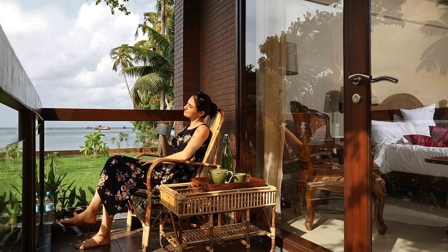 A woman basking in the sun with a mug of hot beverage in the balcony of Lake View Suite and enjoying the view outside