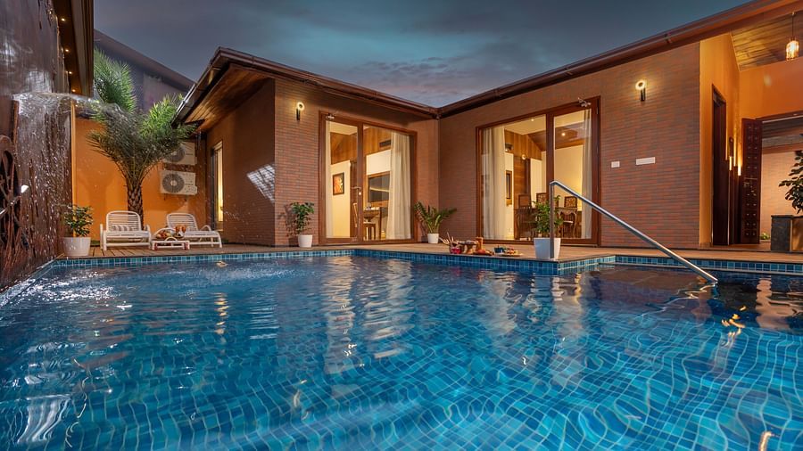 Pool Villa at Uday Backwater Resort featuring a clear swimming pool during late evening reflecting the lights from the villa and a lounge space on the pool deck with bath towels on them