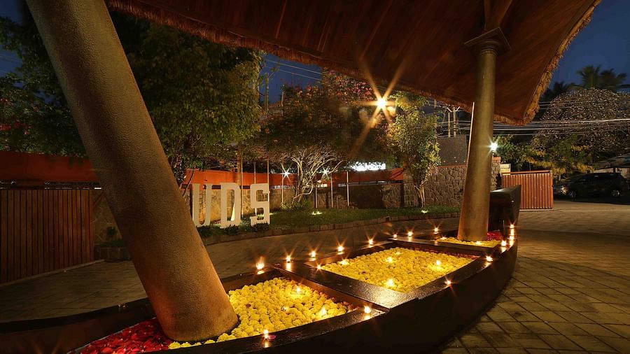 A decorative boat filled with red and yellow flower petals and lit candles enhances the outdoor ambiance of Uday Samudra Leisure Beach Hotel at night.
