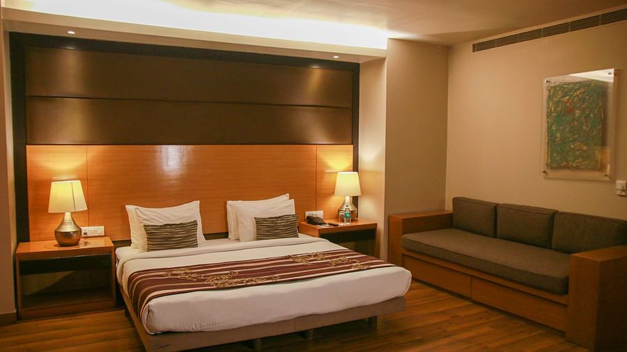 A warm-lit room featuring a king-size bed and two lamps on both sides on the nightstands and a sofa above which a painting is hanging from the wall