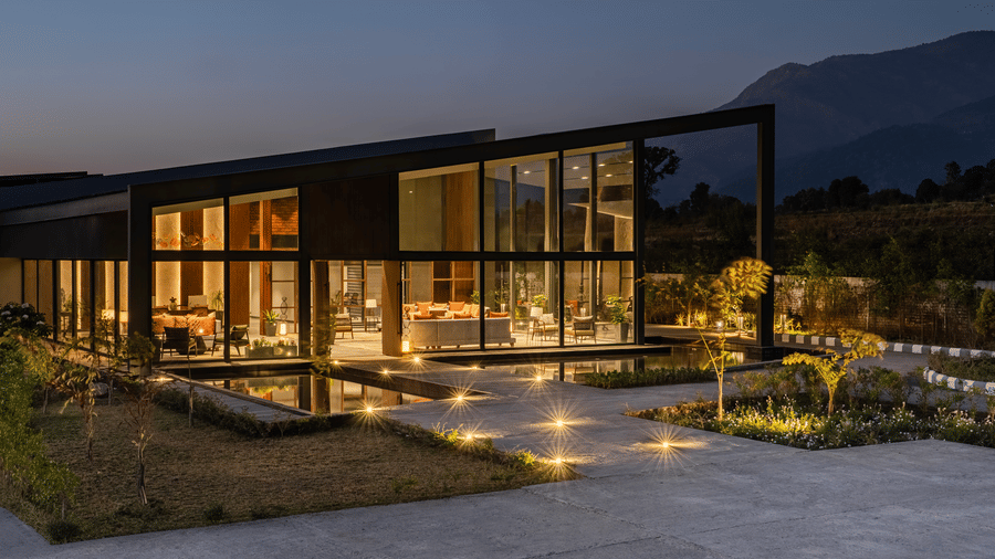 Nighttime exterior of the glass-fronted lobby at Vandhara Sarovar Premiere, Patkote, with warm interior lighting and a stone pathway.
