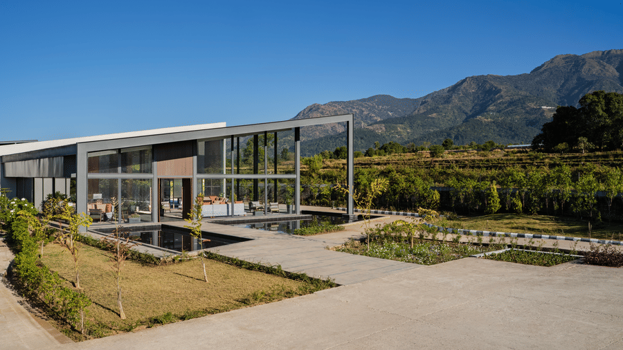 Daytime exterior of the glass-walled restaurant at Vandhara Sarovar Premiere, Patkote, with mountains and green landscaping in the background.