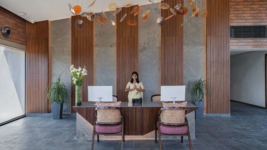 The reception desk at Vandhara Sarovar Premiere, Patkote, featuring a staff member behind a wooden counter with a decorative wall backdrop.