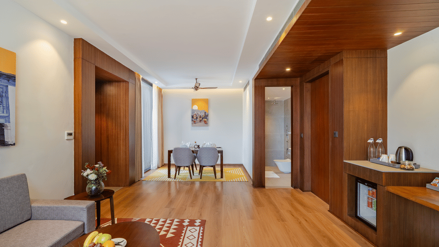 A living and dining space at Vandhara Sarovar Premiere, Patkote, featuring wood flooring, a sofa, and a dining table for 4.