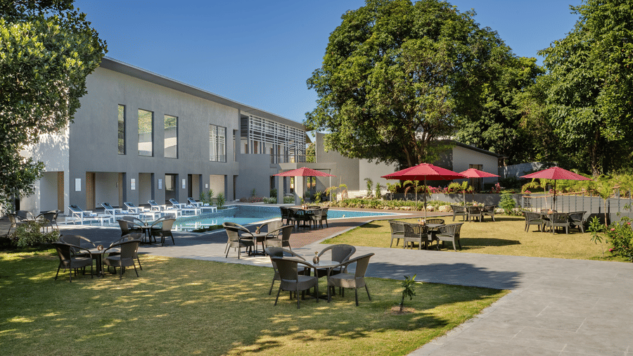 The poolside lawn at Vandhara Sarovar Premiere, Patkote, featuring outdoor dining sets, trees, and a modern two-storey hotel wing.