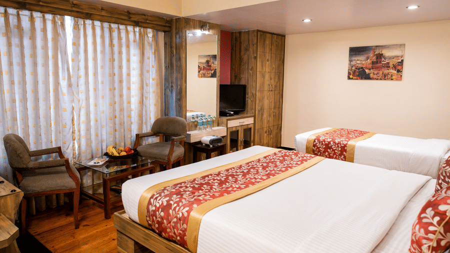 Twin bedroom with red runners, sitting area, fruit basket, and natural light at Viceroy Hotel, Darjeeling.