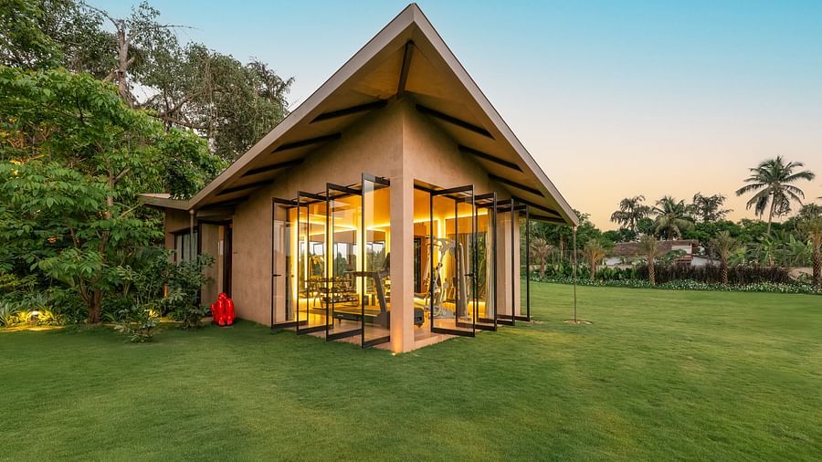 The exterior structure of the gym at Villa Moira by V Escapes, with illuminated glass walls, set on a lush green lawn under a clear evening sky.
