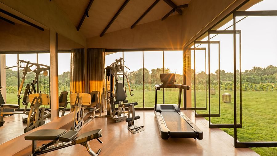 A well-equipped private gym at Villa Moira by V Escapes, featuring modern fitness equipments, large windows, and views of a green outdoor landscape.