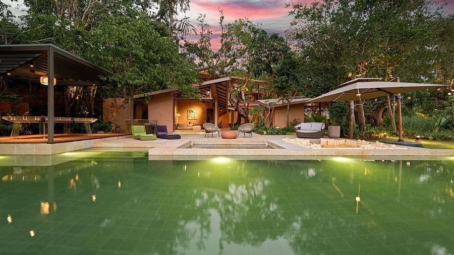  A beautiful evening view of Villa Moira by V Escapes, showcasing the illuminated green pool and the villa's warm lighting under a colourful twilight sky.