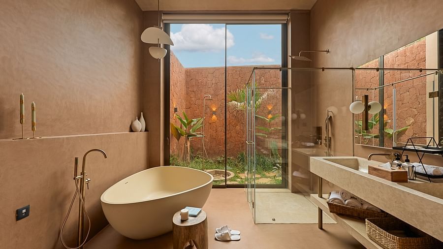 A luxurious bathroom at Villa Moira by V Escapes, showcasing a freestanding bathtub, large window with views, and earthy-toned walls.