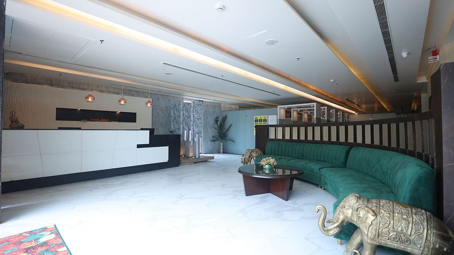A cosy corner with a curved green sofa, round table, and decorative elements in a warmly lit space - VITS Gurugram