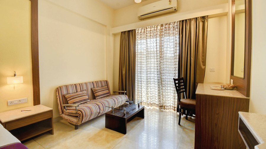 Spacious hotel room with seating area, work desk, and balcony access at VITS Lonavala.