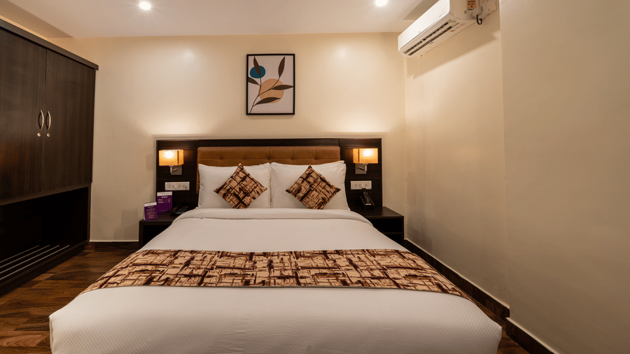 A well-appointed bedroom at VITS Select, Bengaluru, featuring a large bed, side tables, wall art, a wardrobe, and AC, ideal for hotel rooms in Hebbal.