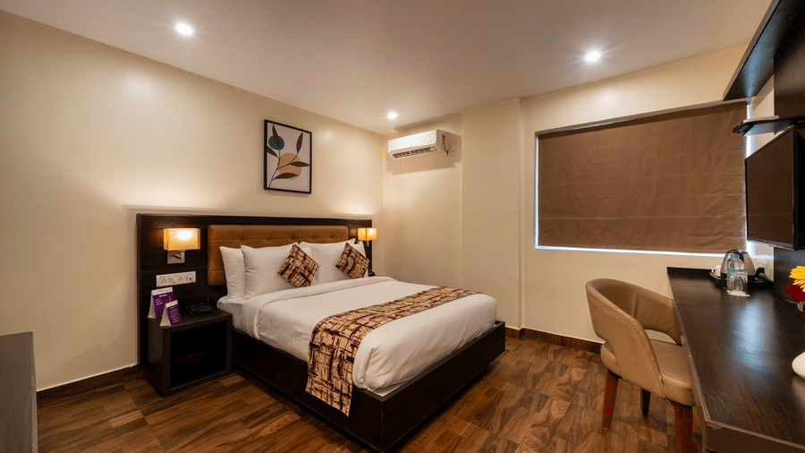 A compact, functional bedroom at VITS Select, Bengaluru, with a comfortable bed, desk, chair, and blinds.