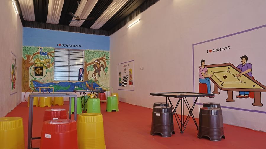 A wide view of a play area at the VITS Select Diamond Resort, Sasan Gir. The room has a red floor, colorful stools, and walls with cartoon-style murals of animals and people playing games.