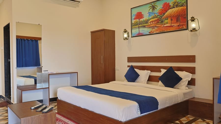 Interior of a room at VITS Select Diamond Resort, Sasan Gir with a double bed, side table, painting, and curtains.