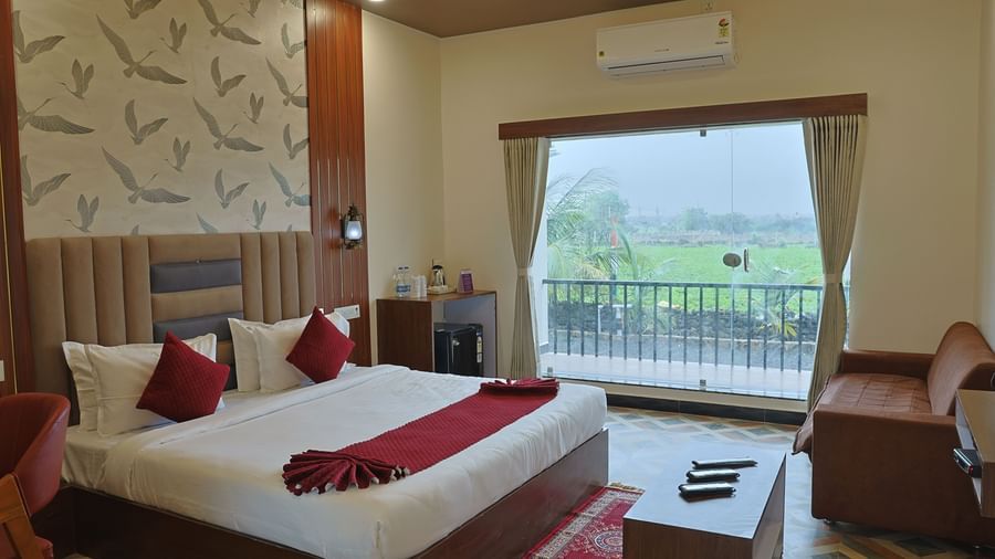 An Executive Room at VITS Select Diamond Resort, Sasan Gir. It includes a bed with a red bed runner, a small sofa, a ceiling fan, and a balcony.