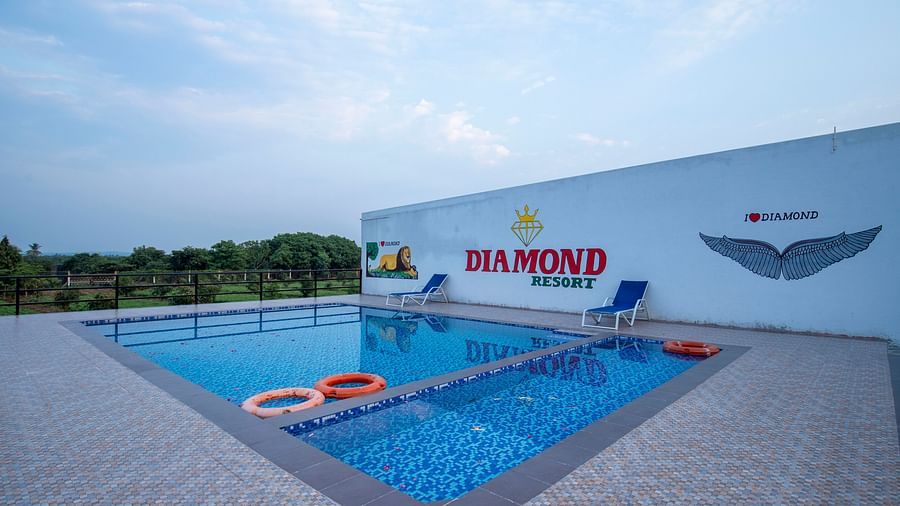 An outdoor swimming pool with clear water and lounge chairs, set against a bright blue sky - VITS Select Diamond Resort, Sasan Gir