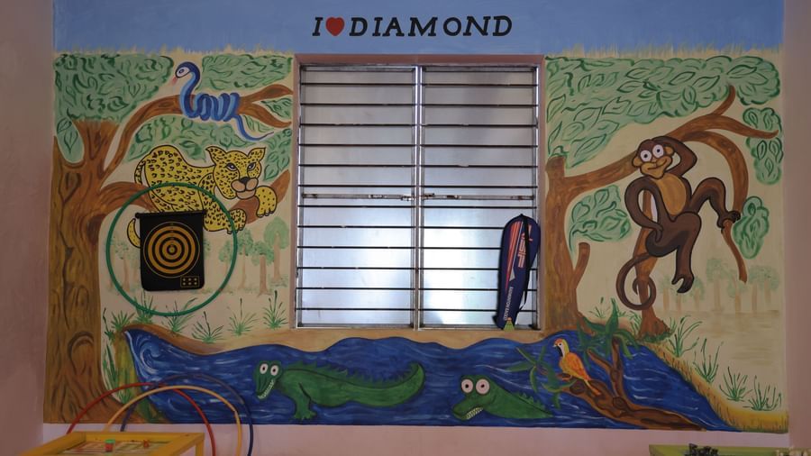 A mural in the VITS Select Diamond Resort, Sasan Gir play area. The painting shows a crocodile and a bird in a blue stream, and a leopard and a monkey in trees, centered around a window.