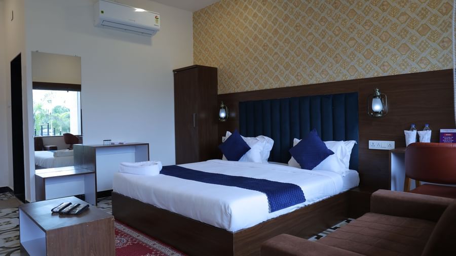 A full view of a Super Deluxe Room at VITS Select Diamond Resort, Sasan Gir. The image shows a bed, a dresser, a wardrobe, and a mirror on a decorative tiled floor.