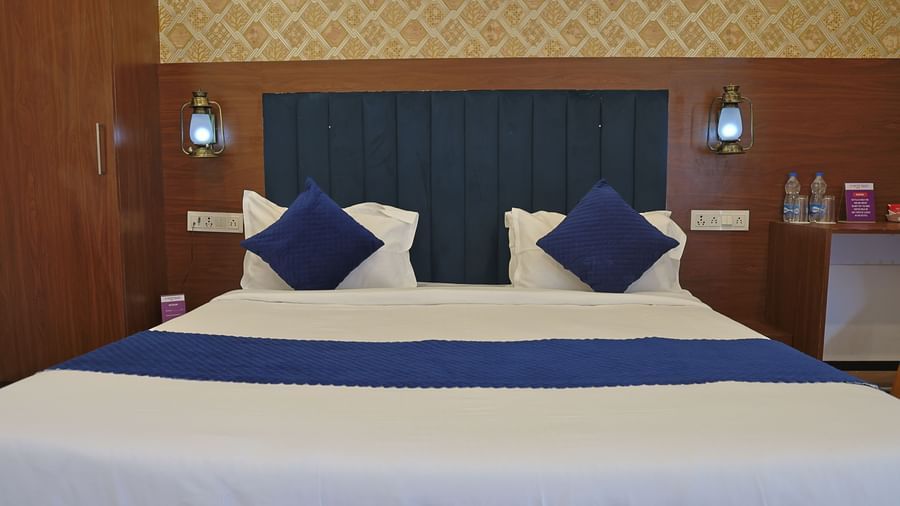 A close-up of a bed at VITS Select Diamond Resort, Sasan Gir. It has a blue upholstered headboard, a blue bed runner, and two pillows with covers.