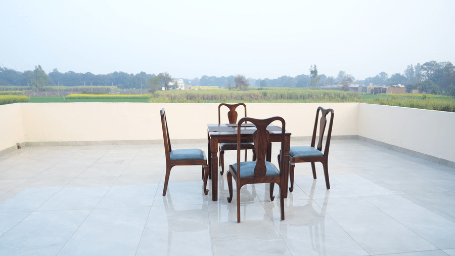 Rooftop terrace with wooden table and chairs overlooking green fields and open surroundings.