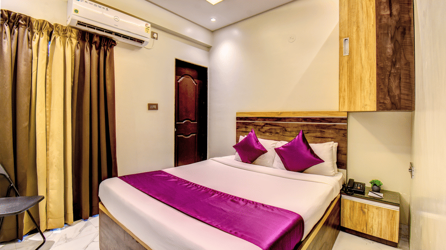 Deluxe Room king bed with purple accent runner, AC unit, gold curtains and wooden wardrobe at VITS Select Kharadi Pune